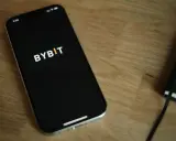 Smartfon z logo Bybit na ekranie, obok notatnik. Analiza bybit prowizje na urządzeniu mobilnym.