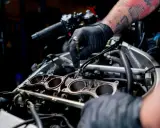 Mechanik w czarnej rękawiczce pracuje przy silniku motocykla, regulując elementy układu chłodzenia.