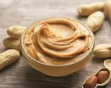 Cremige Erdnussbutter in einer Schüssel, umgeben von Erdnüssen. Ein Beweis dafür, dass erdnussbutter gesund sein kann, wenn sie in Maßen genossen wird.
