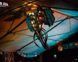 Abstrakte Skulptur mit blauem Gittermuster unter einem Zeltdach, beleuchtet von warmem und kühlem Licht.
