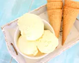 Tres bolas de cremoso helado de vainilla en un cuenco blanco, junto a conos de galleta sobre una bandeja.