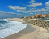 Sonne, Sand und Wellen an der Costa Verde, Portugal. Häuser mit roten Dächern säumen den Strand, geschützt von einer Steinmauer.