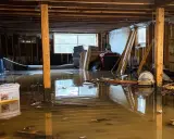 Un **garage inondé** avec de l'eau boueuse recouvrant le sol, des débris flottants et des matériaux de construction endommagés.