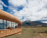 Coppia seduta su una terrazza di **edifici in legno famosi**, con vista su un paesaggio montano e cielo nuvoloso.