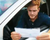 Hombre preocupado mira un papel, preguntándose cuanto tarda una multa en aparecer en mi DGT.