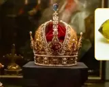 Korona ozdobiona perłami i klejnotami, obok krzyż. W rogu żółty kamień, być może diamenty tekst.