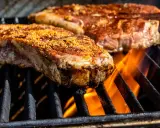Des morceaux de viande savoureux, assaisonnés, grillent sur un barbecue, les flammes léchant les entrecôtes.
