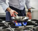 Chef calienta sartén de acero inoxidable para cocinar sobre llama azul de gas.