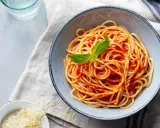 Misternie ułożone spaghetti z sosem pomidorowym i listkiem bazylii. Obok miseczka z tartym parmezanem. Idealne pytanie: jakie przyprawy do spaghetti?