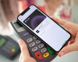 Dłoń zbliża telefon do terminala płatniczego, pokazując ekran Apple Pay. Tak łatwo można płacić telefonem.
