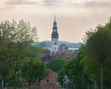 Wieża zegarowa góruje nad zieloną górą, skąd rozciąga się widok na rynek i dachy domów.