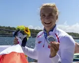Uśmiechnięta sportsmenka z medalem i bukietem kwiatów, symbol sukcesu najlepszych polskich kajakarzy.
