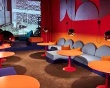 En färgstark lounge med soffor, orange bord och en projektion av Nanna Ditzels design.