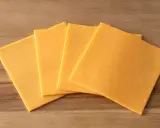 Vier Scheiben gelber Cheddar-Käse, laktosefrei, liegen auf einem Holzbrett.