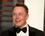 Uśmiechnięty Elon Musk w smokingu z muszką. Wiek nie jest widoczny, ale jego twarz wyraża pewność siebie.