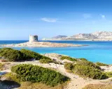 Torre aragonese su isolotto roccioso, mare turchese e macchia mediterranea. Alghero la Pelosa distanza, un sogno sardo.