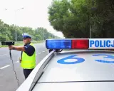 Policjant z radarem na drodze, obok radiowozu z napisem POLICJA.