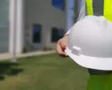 Osoba w kamizelce odblaskowej trzyma biały kask. Dobre technik bhp zarobki to klucz do bezpiecznej pracy.