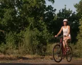 Kobieta w kasku i białej koszulce jedzie na rowerze po leśnej ścieżce. Odkrywa urokliwe trasy rowerowe Wrocławia.