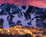 Glitzerndes Aspen, Colorado, im Abendrot. Schneebedeckte Berge mit Skipisten über einer Stadt, die in warmem Licht erstrahlt.