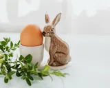 Wielkanocne jajka w kieliszku, obok ceramiczny zajączek i gałązka bukszpanu.