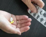 Dłoń trzyma białą i żółtą tabletkę, obok pusty blister. Może to być cytrynian magnezu.