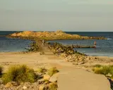 En stenpir leder ut till en klippö. En person går på piren, en annan badar. Perfekt för aktiviteter i Halmstad.
