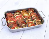 Un plat de tian de légumes, prêt à cuire, avec des rondelles de courgettes, aubergines et tomates joliment disposées. Parfait pour faire un tian de légumes la veille.