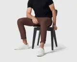 A man in a black shirt and brown pants sits on a black chair, wearing white sneakers.