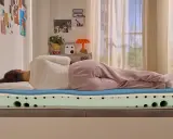 Frau liegt auf einer Emma Matratze, die zu hart erscheint. Die Schichten der Matratze sind sichtbar.