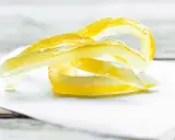 Gelbe Zitronenschalen-Streifen, die an das Selbermachen von Apfelpektin erinnern, liegen auf weißem Papier.