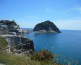 Scogliere a picco sul mare blu, case bianche aggrappate alla costa e un isolotto verde. Un paesaggio che ispira frasi su Ischia.