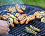 Grilla korv med grönsaker på en kolgrill. Röken stiger från den saftiga maten.
