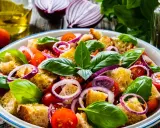 Panzanella ricetta: un'insalata estiva con pane raffermo, pomodorini, cipolla rossa e basilico fresco, condita con olio d'oliva.