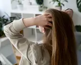 Kobieta sprawdza swoje długie, brązowe włosy, zastanawiając się, jak mieć gęste włosy.