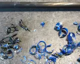 Metalowe przelotki do wędki leżą na szarym blacie, obok niebieskich wiórów i kawałków plastiku.