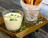 En krämig creme fraiche sås med örter serveras bredvid en glasbehållare med krispiga pommes frites på ett rustikt träbord.