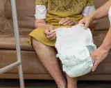 Opiekunka pomaga starszej osobie założyć pieluchę, zapewniając komfort i zabezpieczenie przed ściąganiem pampersa.