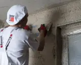 Pracownik w białej czapce i rękawiczkach gąbkuje tynk. Czas na gąbkowanie tynku zależy od jego rodzaju i warunków.
