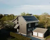 Ett modernt hus med mörk fasad och ett tak täckt av solceller. Bredvid huset finns ett garage med vita portar.
