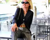 Donna con pantalone grigio elegante, abbinato a cardigan scuro e cintura con logo dorato. Un look chic per ogni occasione.