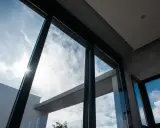 El sol brilla a través del vidrio guardian, iluminando un cielo azul con nubes blancas.