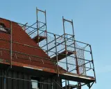 Metalowe rusztowanie na dachu z czerwonej dachówki, gotowe do prac remontowych.
