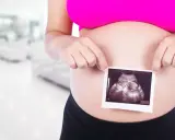 Ciężarna kobieta trzyma zdjęcie USG płodu na tle rozmazanego wnętrza.