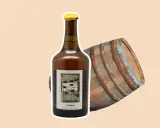 Bouteille de vin jaune à côté d'un vieux fût de chêne. Le vin jaune, une spécialité du Jura, est un vin oxydatif unique.