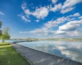 Passeggiata in legno sul **lago di Chiusi**, con cielo azzurro e nuvole bianche che si riflettono sull'acqua calma.
