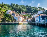 Un pintoresco pueblo costero con **5 villas** coloridas apiladas en una colina verde, frente a un mar turquesa.