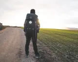Pellegrino solitario su un sentiero sterrato, con un campo verde a destra. Le sue cammino di Santiago esperienze negative sono un ricordo lontano, mentre il sole tramonta.
