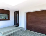 Ingresso con porta scura e avvolgibili marroni, accanto a un'ampia porta garage in legno scuro.