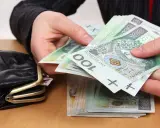 Dłonie liczą banknoty 100 zł obok portmonetki. Zastanawiasz się, ile wynosi trzynasta emerytura netto?
